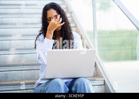 Eine Frau, die Stress erlebt, arbeitet an ihrem Laptop in einem modernen, stilvollen Innenbereich Stockfoto
