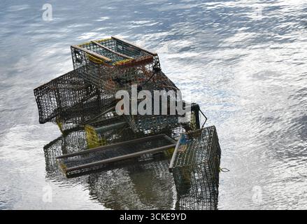 Haufen von ausgemusterten Hummerfallen sind halb mit Meereswasser vor der Küste von Maine bedeckt. Die Fallen sind aus Stahl und übereinander gestapelt. Stockfoto
