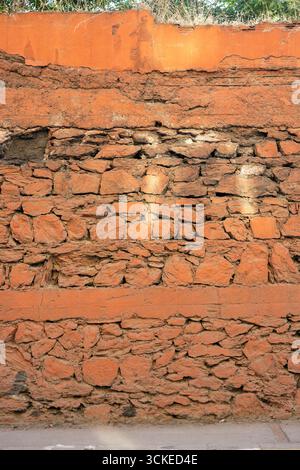 Oranger alter Stein und Ziegelmauer mit wilden Pflanzen – rustikale urbane Textur, verwitterte Steinmauer mit orangem Gips und Vegetation ustikales Mauerwerk mit Gr Stockfoto