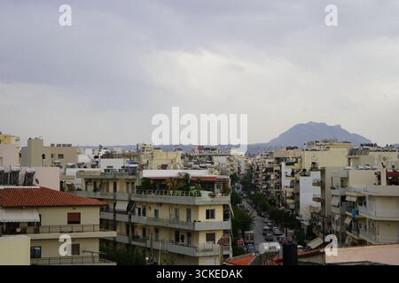 Ein erhöhter Blick auf die dichte Stadtlandschaft von Heraklion mit einem Berg an einem bewölkten Tag, der einen Einblick in das Leben der Inselstadt bietet. Stockfoto