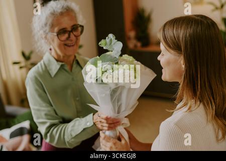 Ältere kaukasische Frau lächelt, während sie Bouquet von der jungen Erwachsenen erhält Stockfoto
