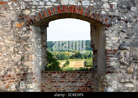 Ein rustikaler Steinbogen in einer Ruine umrahmt Felder, Bäume und ferne Hügel wie ein Naturfenster. Verbindet architektonisches Erbe mit pastora Stockfoto