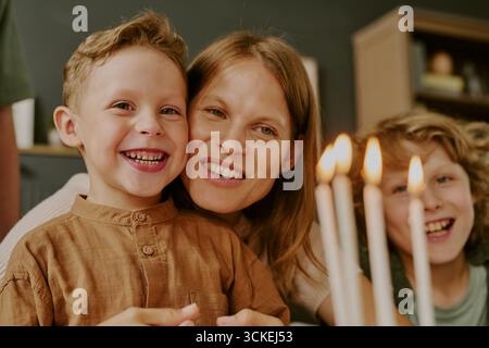 Porträt der kaukasischen Mutter mit zwei Kindern, die in der Nähe von Geburtstagskerzen lächeln Stockfoto