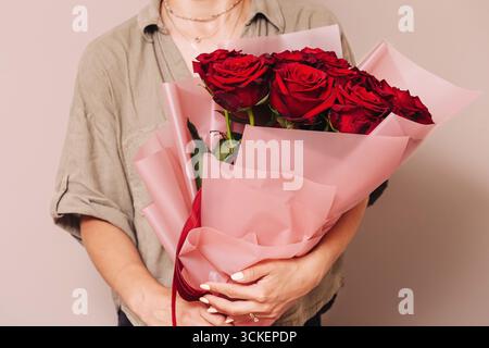 Frau mit einem Strauß roter Rosen. Romantisches Geschenk in Papier. Blumenarrangements zum Feiern. Stockfoto