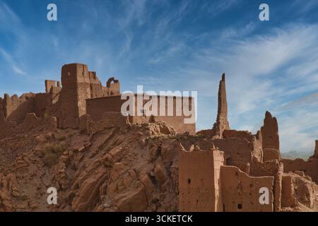 Alte marokkanische Ksar-Ruinen - Eine weite Aufnahme der Ruinen eines traditionellen befestigten Dorfes (ksar) in Marokko, erbaut mit Lehmziegeln auf einem Hügel unter einem b Stockfoto