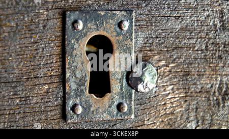 Nahaufnahme eines alten, leicht verrosteten Schlüssellochs in einer Holztür Stockfoto