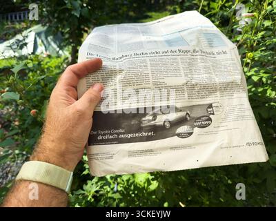 Paris, Frankreich - 12. August 2025: Hand hält eine deutsche Vintage-Zeitung mit Toyota Corolla Werbung und Artikeln im Freien Stockfoto