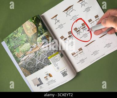 Paris, Frankreich - 2. September 2025: Handmarkierung Katalogseite mit rotem Stiftkreis um hölzerne Gartenmöbel auf grünem Hintergrund deutscher Katalog Stockfoto