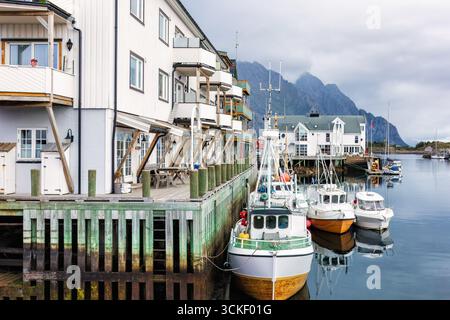 Fischerdorf Lofoten Inseln mit farbenfrohen Booten, die entlang des hölzernen Piers angedockt sind, umgeben von malerischen Bergen und traditioneller Architektur Stockfoto