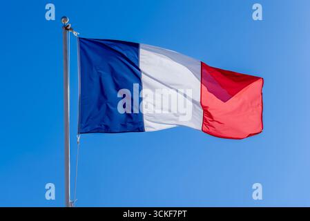 Französische Nationalflagge mit blauen, weißen und roten Farben winkt im Wind vor einem klaren blauen Himmel Stockfoto