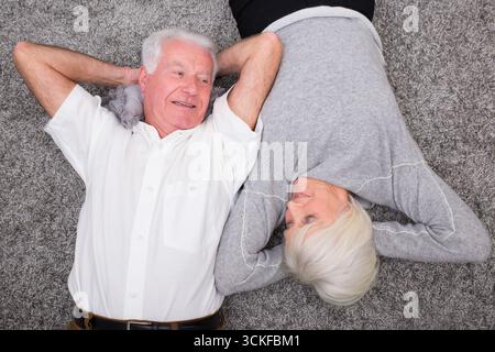 Seniorenpaar, das zu Hause auf dem Teppich im Wohnzimmer chillt Stockfoto