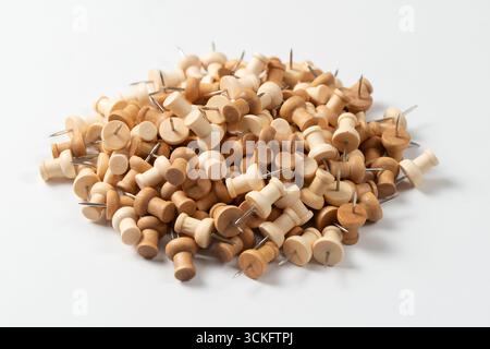 Ein großer Stapel von Holzstiften oder Daumenstiften auf einem sauberen weißen Hintergrund. Die Stecknadeln haben eine natürliche Holzmaserung und verschiedene Brauntöne. Stockfoto