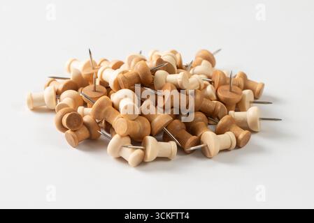 Ein großer Stapel von Holzstiften oder Daumenstiften auf einem sauberen weißen Hintergrund. Die Stecknadeln haben eine natürliche Holzmaserung und verschiedene Brauntöne. Stockfoto