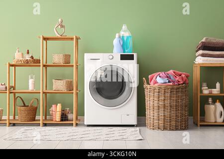 Moderne Waschmaschine, Regal und Korb mit Waschmaschine im Zimmer Stockfoto