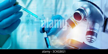 Nahaufnahme der Wissenschaftlerhand mit Pipette, die blaue Flüssigkeit unter dem Mikroskop im Forschungslabor in das Reagenzglas tropft, was die Biotechnologie symbolisiert, Medica Stockfoto