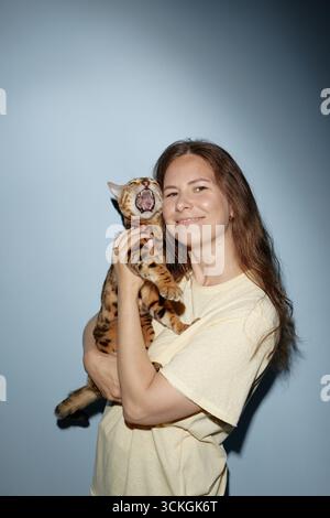 Junge Frau, die Bengale Katze lächelnd hält, während Katze Gähnen ist Stockfoto