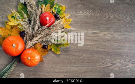 Herbstarrangement mit Kürbissen und Blättern auf Holzoberfläche. Ein schönes flaches Arrangement mit leuchtenden orangefarbenen Kürbissen, gelber Herbst Stockfoto