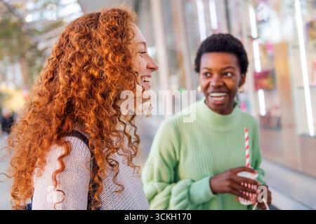 Zwei junge Frauen lachen, während sie auf der Straße reden Stockfoto