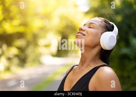 Entspannte schwarze Frau in Sportbekleidung, die beim Laufen im Freien Musik mit Kopfhörern genießt Stockfoto