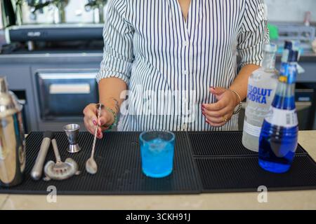 Crema, Italien - 25. August 2025 Ein Barkeeper bereitet an einer Bar einen lebhaften blauen Cocktail zu, der erfrischende alkoholische Getränke für Gäste mischt Stockfoto
