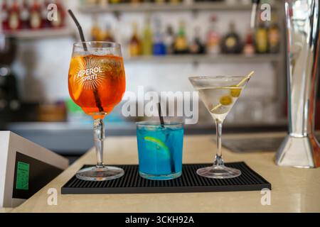 Crema, Italien - 25. August 2025 drei farbenfrohe Cocktails, die kunstvoll auf einer Bar-Countertop arrangiert werden, um die Gäste in einem lebhaften Abendgesellig zu servieren Stockfoto