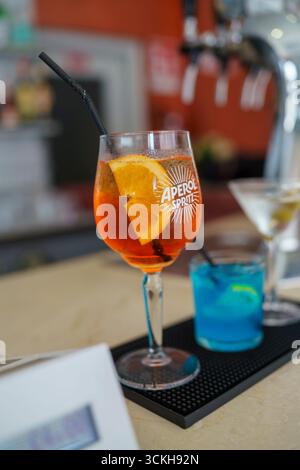 Crema, Italien - 25. August 2025 erfrischender Aperitif-Cocktail in leuchtendem Orange, garniert mit frischem Zitrusstück und dunklem Strohhalm an einem Bartheken mit Soft Stockfoto