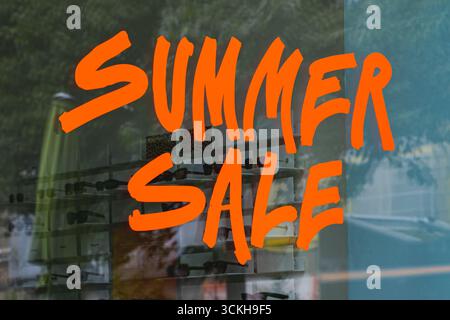 Leuchtend orangefarbenes Sommerschild in moderner Freihandschrift an einem Schaufenster Stockfoto