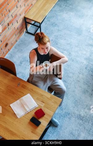 Blick von oben auf die Frau, die sich mit einem Heißgetränk in der modernen Inneneinrichtung entspannt. Stockfoto