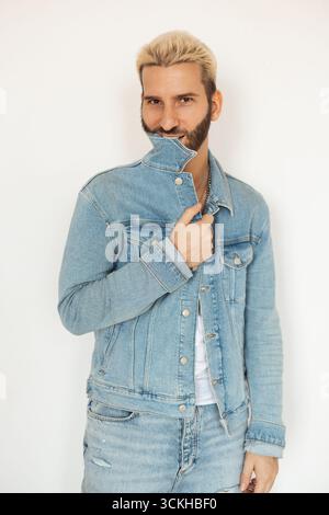 Stilvoller Mann, der mit einer Jeansjacke auf weißem Hintergrund posiert Stockfoto