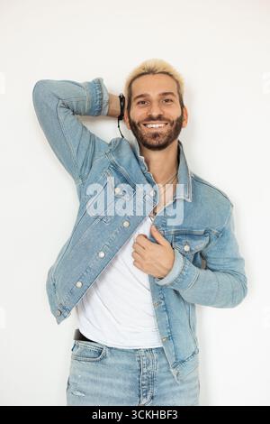 Modischer Mann posiert selbstbewusst in einer Jeansjacke vor der weißen Wand Stockfoto
