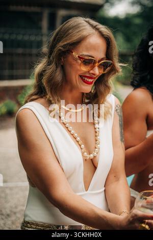 Stilvolle Frau mit Sonnenbrille und Schmuck, die draußen lächelt Stockfoto