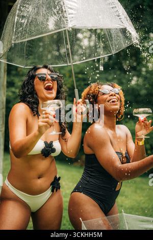 Zwei Frauen lachen unter Regenschirm und halten Cocktails Stockfoto