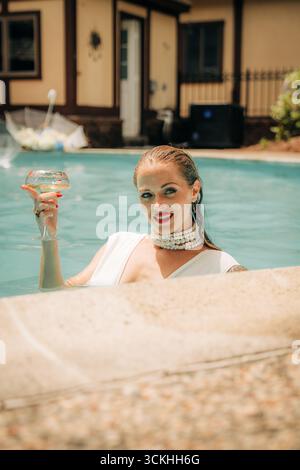 Influencer, der sich in einem Pool entspannt und ein Cocktailglas hält Stockfoto