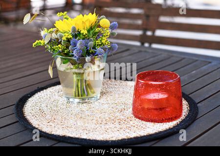 Nahaufnahme von gelbem und lila Blumenstrauß und Sturmlampe mit Kerzendekoration auf dem Tisch Stockfoto