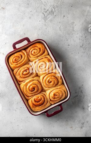Frisch gebackene zimtbrötchen in einer Keramikform auf hellgrauem Hintergrund, isoliert von oben, Textraum. Zimtrollen herstellen. Vertikal Stockfoto