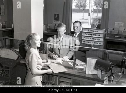 Das Innere einer Bank mit einer jungen Frau an der Theke, die den Kunden hilft. 1949. Kristoffersson Ref. AO9-8 Stockfoto