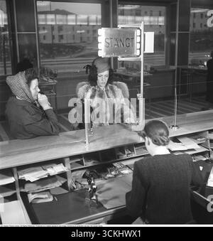 Das Innere einer Bank mit einer jungen Frau hinter dem Tresen im Bankbüro. Sie wird gesehen, wie sie einem Kunden hilft, der am Kassenschalter steht. Das Bild symbolisiert die Finanzgeschichte und die persönliche Sparkultur und ruft Nostalgie für traditionelle Bankpraktiken hervor. 1949. Kristoffersson Ref. AN34-3 Stockfoto