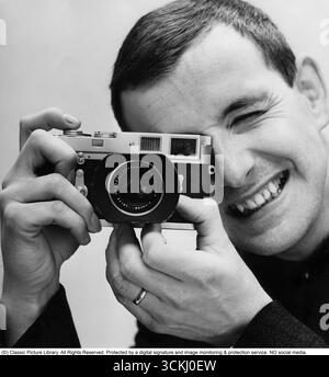 Fotograf in den 1960er Jahren Ein Mann hält seine Kamera an sein Auge und fokussiert sich. Die Kamera verwendet Film ist vollständig analog. 1965 Stockfoto