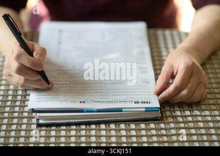 Eine pensionierte Frau, die ein Steuerdokument aus dem Jahr 1040 sorgfältig überprüft und sich dabei auf die persönliche Finanzierung zu Hause konzentriert Stockfoto