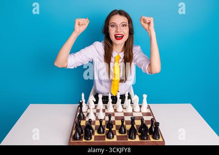 Junge Frau, die sich im Schach auszeichnet, unterstreicht akademische Fähigkeiten in einer stilvollen Umgebung mit einem fröhlichen und selbstbewussten Ausdruck Stockfoto