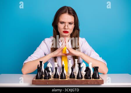 Kluge, kompetente Frau, die sich intensiv darauf konzentriert, einen Schachzug auf einem Brett zu planen, indem sie Intelligenz und Konzentration unter Beweis stellt. Stockfoto