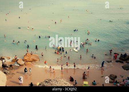 Eine überfüllte Strandszene mit Menschen, die im ruhigen türkisfarbenen Wasser schwimmen und entspannen, die Sommersonne und das Sandstrand zusammen genießen Stockfoto