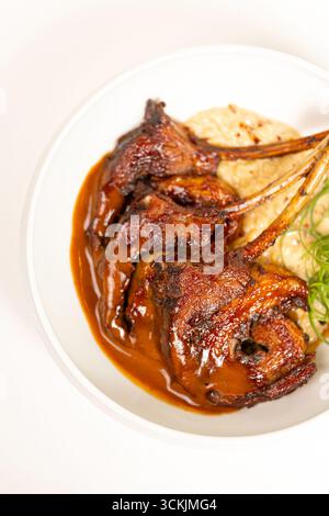 Detaillierte Nahaufnahme gerösteter Lammrippchen mit kräftiger brauner Sauce und Kräutern, fotografiert vor weißem Hintergrund für kulinarische Projekte und kulinarische Projekte. Stockfoto