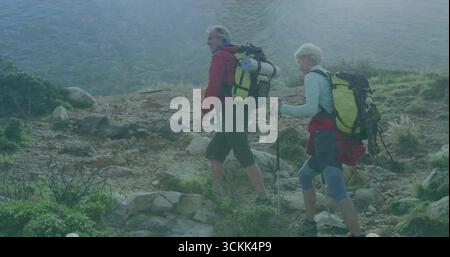 Klettern Sie auf einem felsigen Wanderweg am See, mit Rucksäcken und Trekkingstöcken Stockfoto