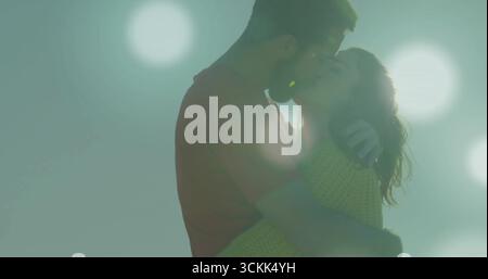 Ein küssendes Paar, das sich unter dem trüben Himmel umarmt mit schwebenden Lichtkugeln, Strickpullover und T-Shirt trägt Stockfoto