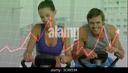 Radspaar in sportlicher Kleidung, das im Fitnessstudio auf Fahrrädern radelt, mit rotem Graphen-Overlay Stockfoto