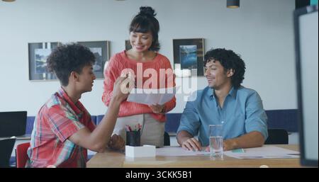 Asiatische Frau mit gedruckten Karten und Stift im Besprechungsraum, während Kollegen zuhören Stockfoto