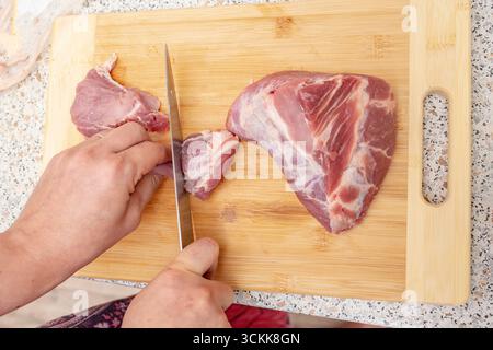 Frau schneidet rohes Schweinefleisch auf einem hölzernen Schneidebrett Stockfoto