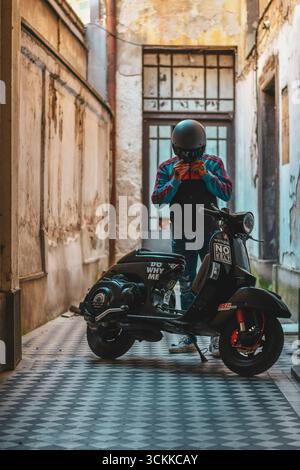 Mann sitzt auf einem schwarzen Vespa-Roller in einem alten Innenhof, Belgrad, Serbien Stockfoto