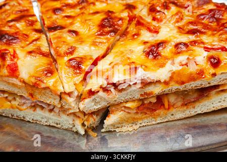 Geschnittene Pizzascheiben auf einem Tablett mit viel Käse, Nahaufnahme. Stockfoto